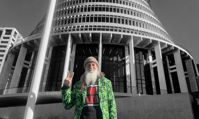 An older gentleman stands in front of the beehive wearing a suit covered in cannabis leaves.