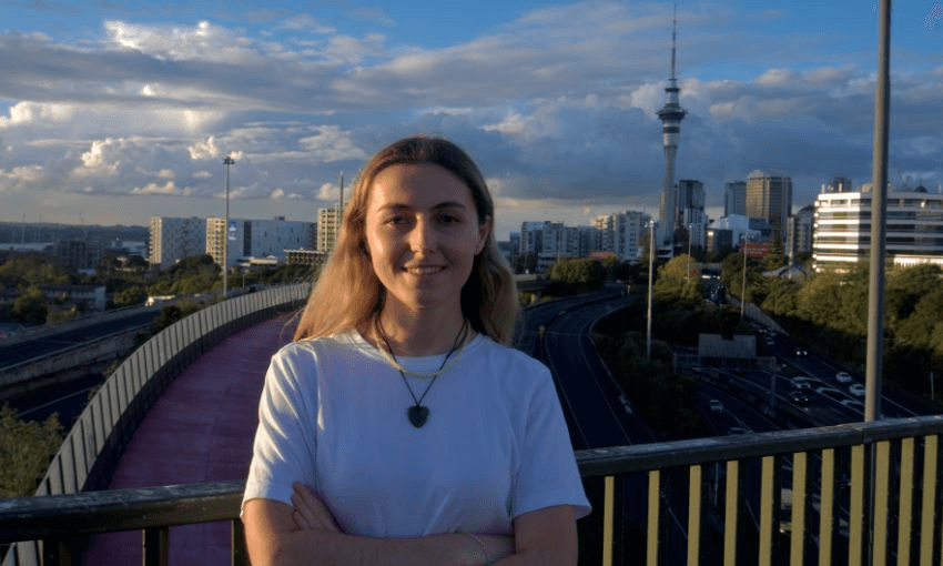 Caitlin Wilson standing, arms folded, on Auckland's Hopetoun Street Bridge with the Skytower in the background.