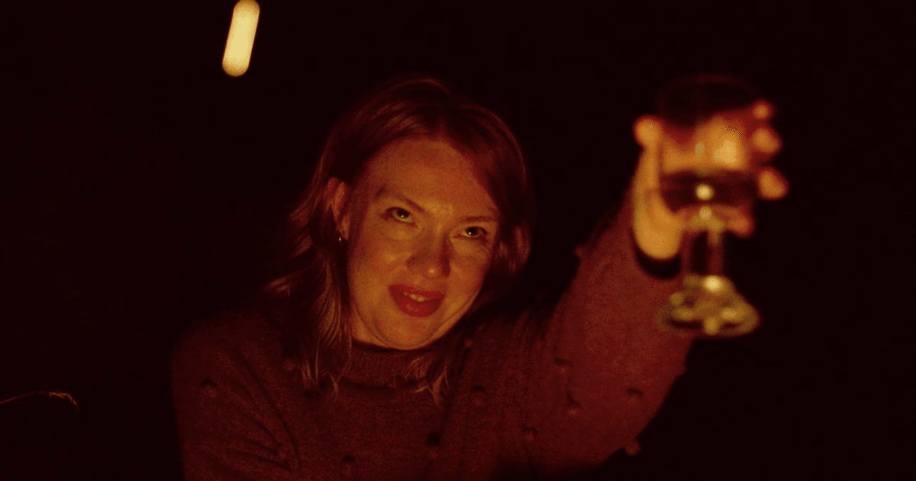 A woman with fire reflected on her face raises a glass of red wine
