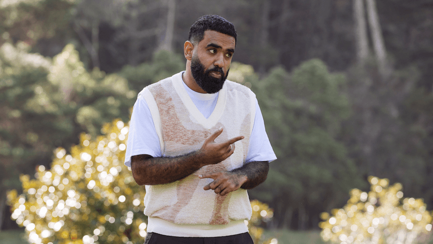 Pax Assadi wears a cream vest and points at Paul