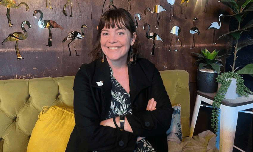 Julie Anne Genter, sitting on a green couch with her arms folding and grinning.