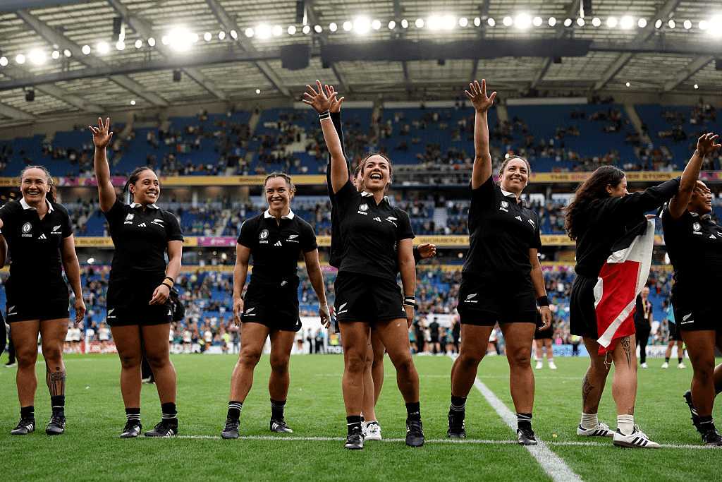 Five rugby players wave to a stadium crowd from the field, smiling