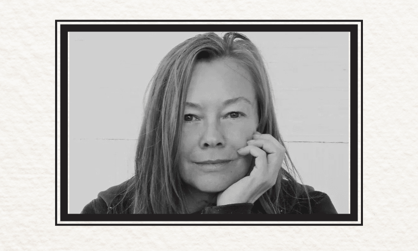 A black and white photo of Kelly Ana Morey who has shoulder length hair and has her hand to her face. She is looking at the camera.