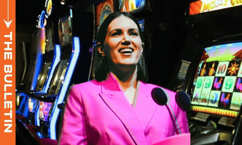a woman (Brooke van Velden) speaks into a microphone wearing a pink suit with a background of pokie machines.