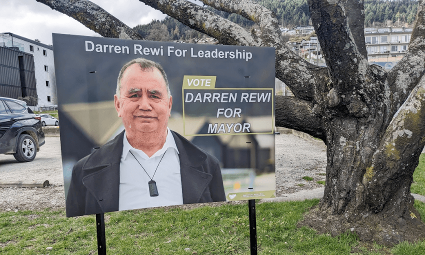 a serious looking Māori man with a sign saying "darren Rewi For Leadership"