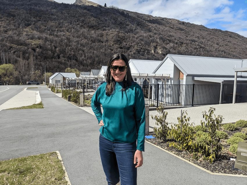 a middle aged white mowan in a green shirt with some small houses that have been newly completed in the background