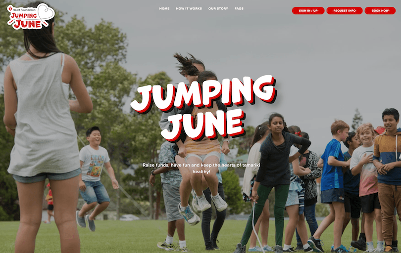 Children jump rope and play together on a grassy field, smiling and laughing. The text "Jumping June" appears in bold letters, with navigation buttons and a logo at the top of the image.