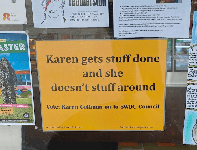 A yellow campaign poster on a window reads: "Karen gets stuff done and she doesn’t stuff around. Vote: Karen Coltman on to SWDC Council." Other posters are partially visible around it.