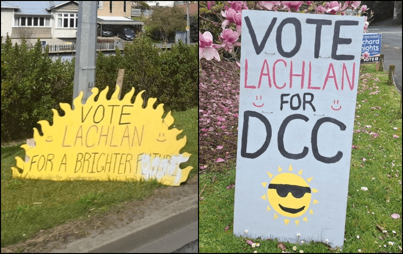 Two roadside campaign signs read "Vote Lachlan for a brighter future" and "Vote Lachlan for DCC," featuring cheerful sun illustrations and handwritten text, placed on grassy areas beside the road.