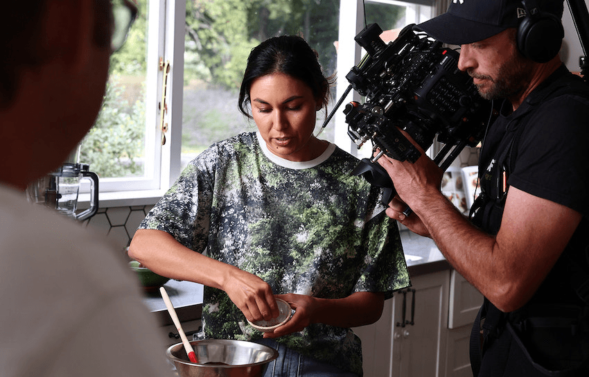 Nadia Lim mixes something in a silver bowl while a camera man films her hand's close up 