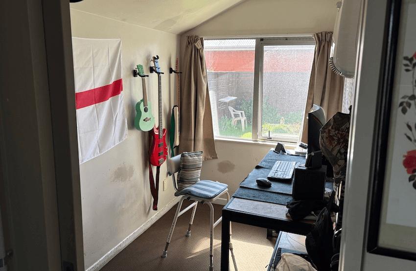 A small grey office with a mint green ukulele, red guitar, and United Tribes flag hanging on the wall. There is a repurposed hospital seat and computer against the other wall