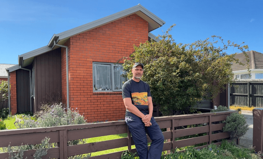 Rob stands against the front fence of the brick property
