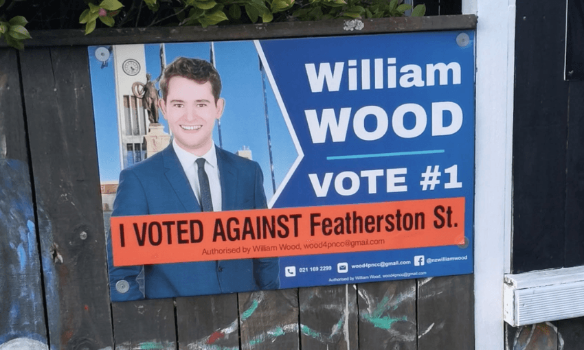 a blue nationalish sign with a young man in a suit and the words 'I voted AGAINST featherston St"