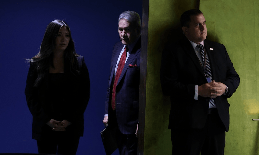 Three people in business attire stand indoors, partially separated by a wall; two are in shadow on the left, and one stands in light on the right, all with serious expressions.