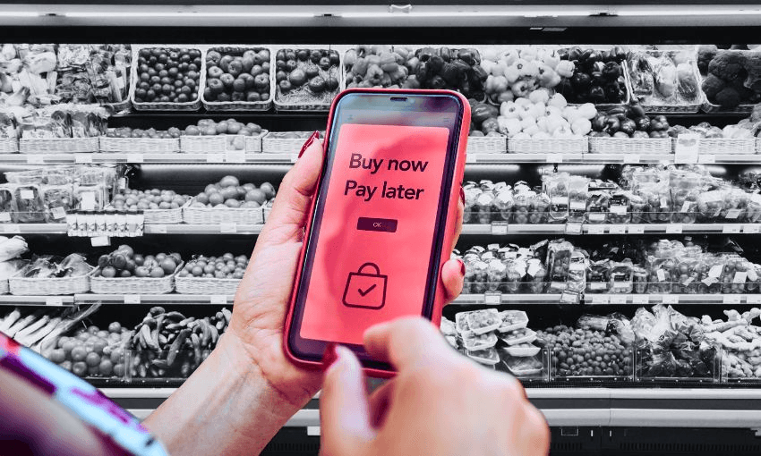 A phone displaying "buy now pay later" on its screen, super imposed in front of a grocery aisle.