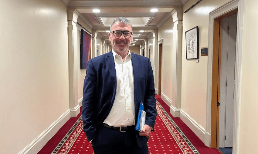 Duncan Webb stands and smiles in the middle of a hallway in parliament.