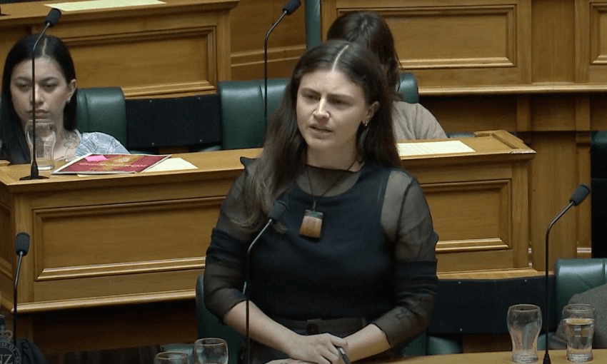 Chloe Swabrick stands in the House with her hands folded over each other on her desk.