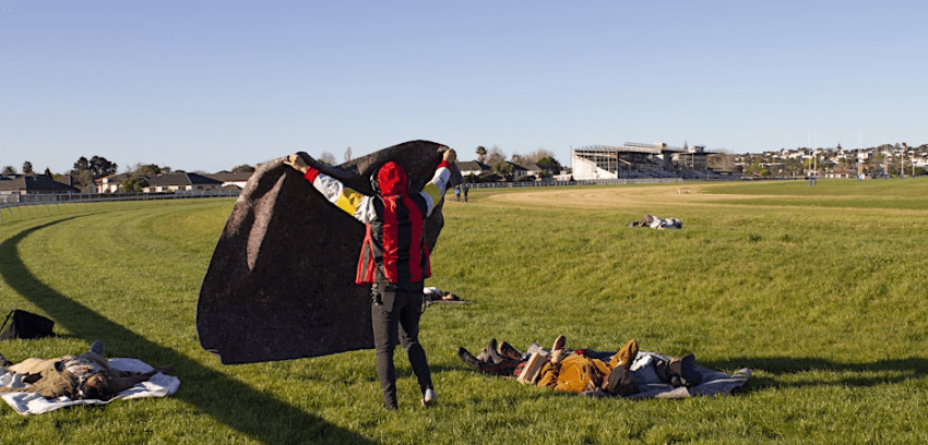 A photograph of a racecourse with people spreading a blanket on the ground as if to have a picnic. 