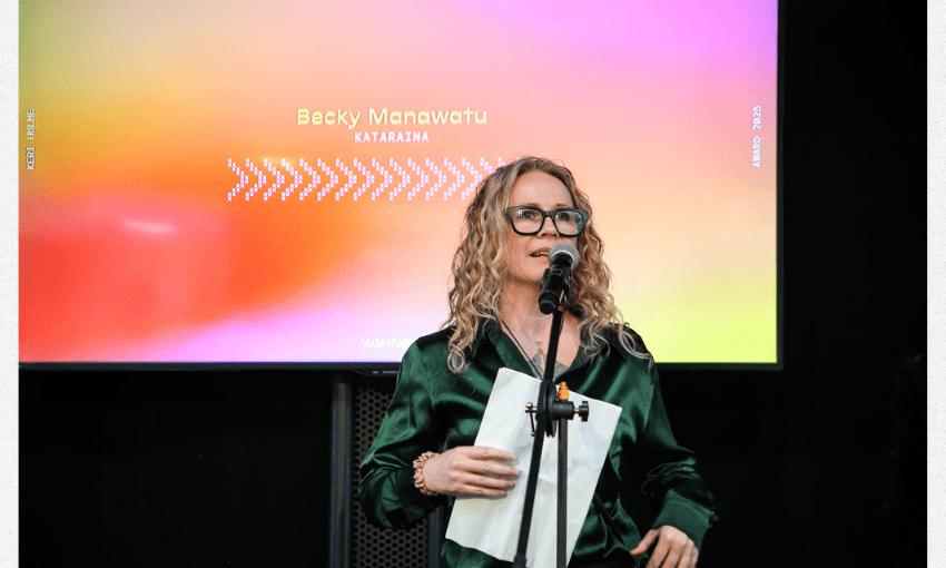 A photo of Becky Manawatu on a stage at a microphone speaking. 