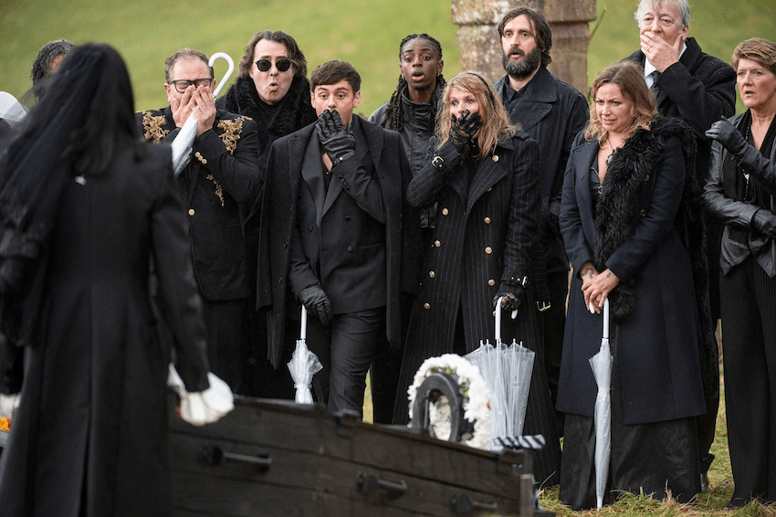A group of funeral mourners gasp in front of an open coffin