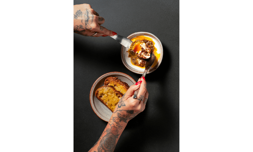 A photograph from above of a plate of toasted sourdough bread and a plate of eggs. A pair of hands is tucking into the eggs. 