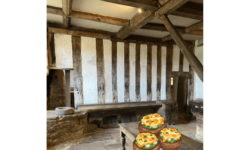 A photograph of a medieval kitchen with an illustration of three stuffed potatoes layered onto the table in the photo.
