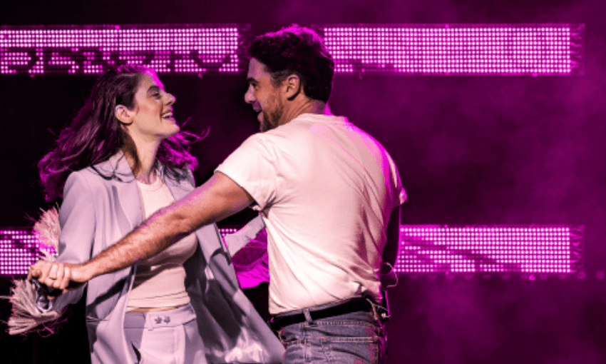 A photograph of the actors in Heartbreak Hotel (a theatre show) on stage which is lit with pink. they are holding hands and are in active poses almost as if they are dancing. 