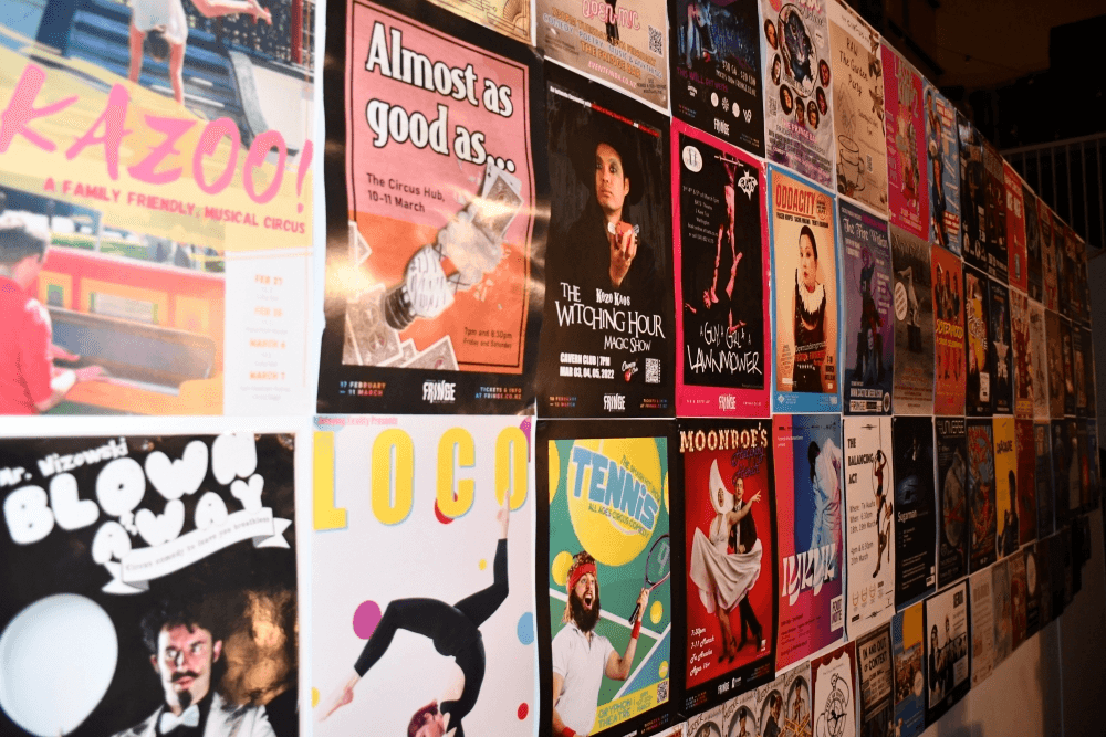 A wall covered with colorful posters promoting various theatre, music, and circus events, each featuring unique designs, images, and bold text.