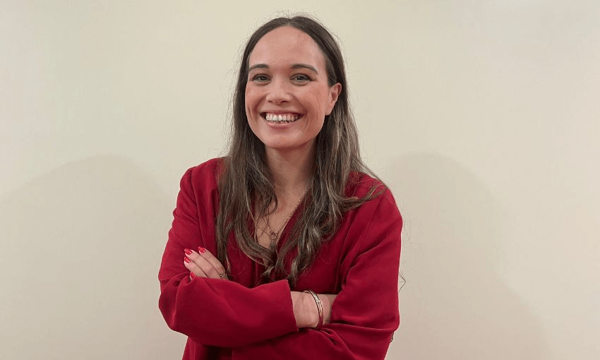 Wearing an all red ensemble, Arena Williams stands with her arms folded across her chest in front of a white wall.