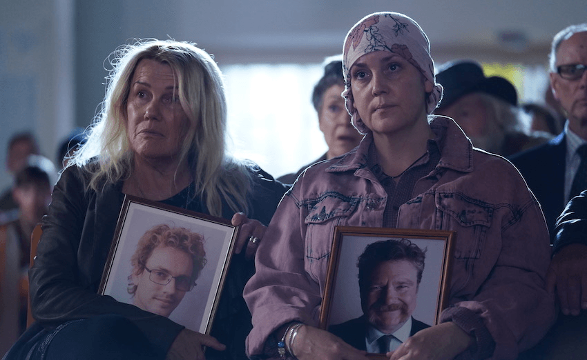 Two women sit in a church pew holding framed photographs of men. 