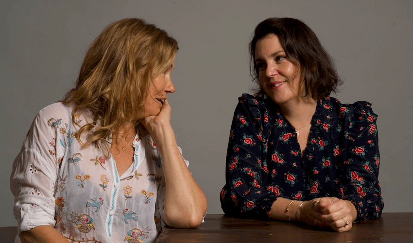 Robyn Malcolm and Melanie Lynskey smile at each other in floral shirts against a grey background