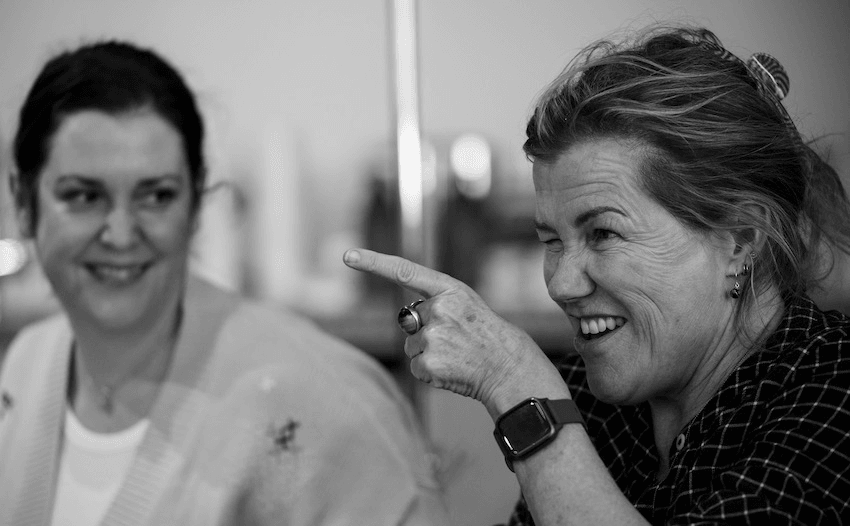 A black and white image of Robyn Malcolm and Melanie Lynskey smiling during rehearsals