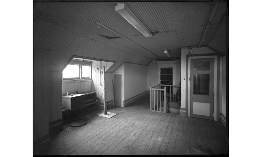 A black and white photo of the interior of a house: the attic space showing windows, columns and not much else. 