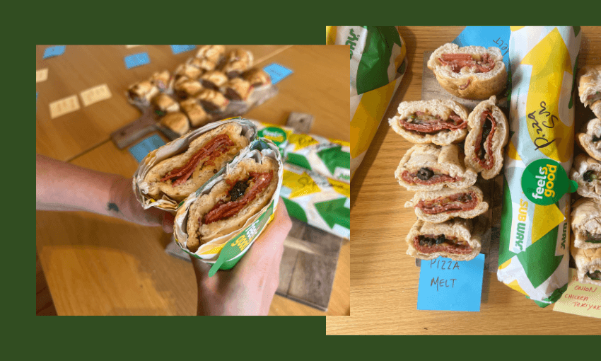 Two hands hold a halved Subway sandwich filled with meat, cheese, and sauce. Nearby, sliced Subway sandwiches are labeled with tags like "Pizza Melt," all displayed on a wooden table.