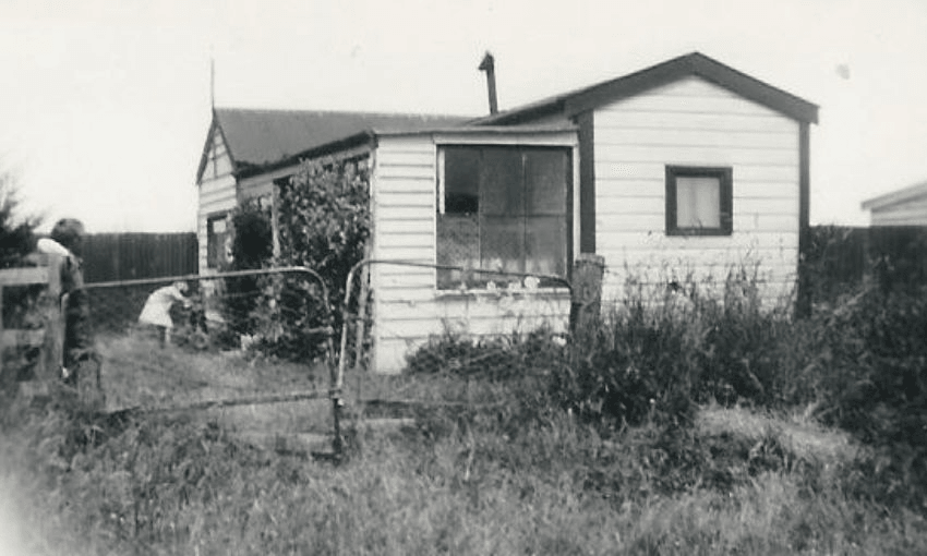 A black and white photograph of Fionna Hill's family hut in Milford, surrounded by tall grass.