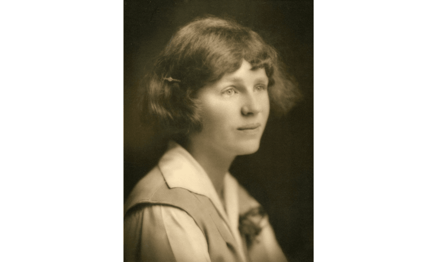 A sepia photo of writer Robin Hyde, she has short hair and is wearing what looks like a uniform. She is gazing out into the distance.