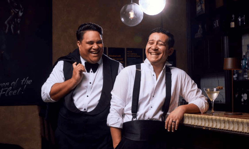 Two men in suits, with jackets off, laughing. 