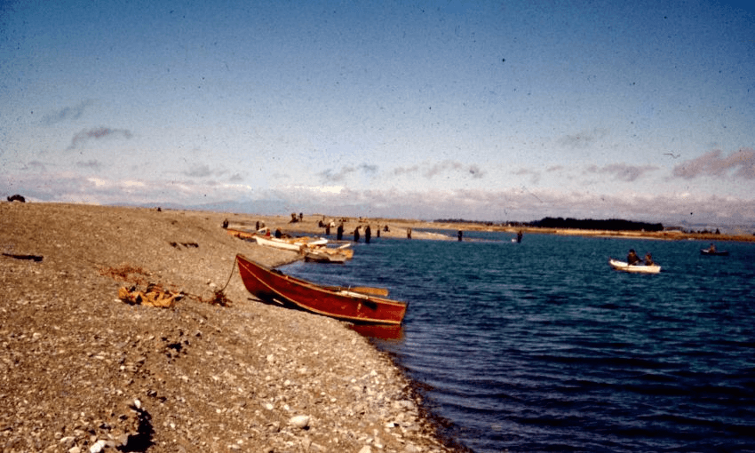 An old photograph of Ōpihi Bay, with boats moored at the shore and individuals in the sand and waters.