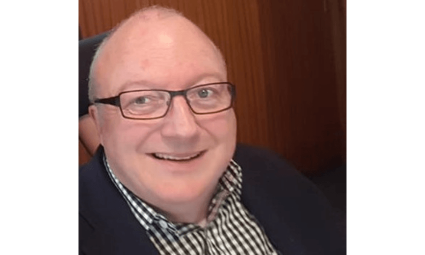 a smiling pakeha man in a power chair with a checked shirt on