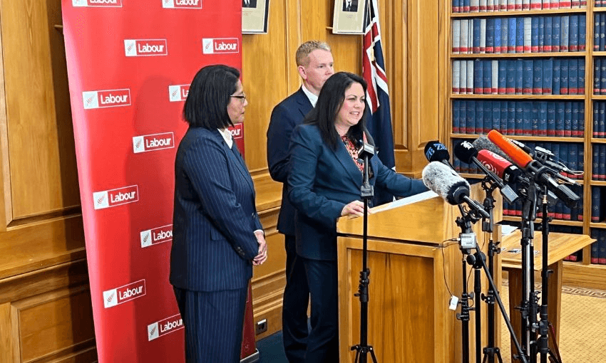 Ayesha Verrall stands at a podium, speaking into microphones in front of a Labour Party banner. Beside her are Barbara Edmonds and Chris Hipkins.