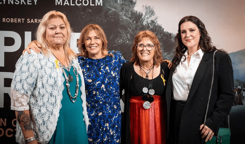 A photo against a Pike River press wall with four women standing arm in arm