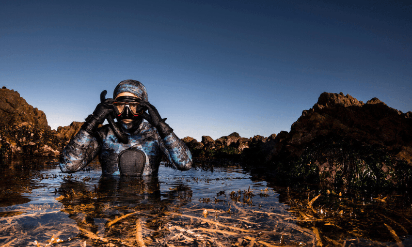 a person in a wetsuit with rocks and a dark sky around her 