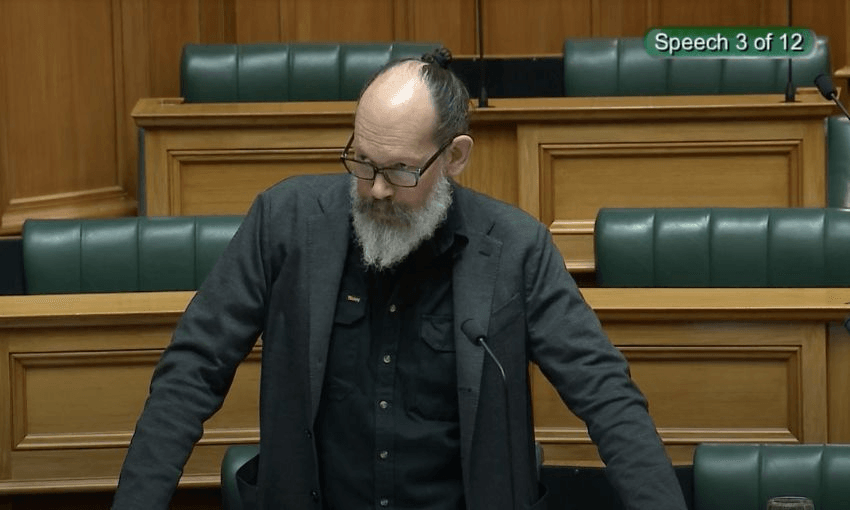Steve Abel, leaning over his desk, speaks to the House on the MACA bill.