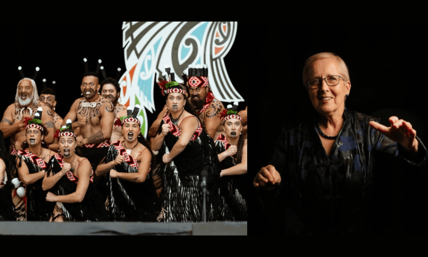 A group of Māori performers in traditional dress and face paint pose energetically on stage, while an older woman in glasses and dark clothing gestures with her hand against a black background.