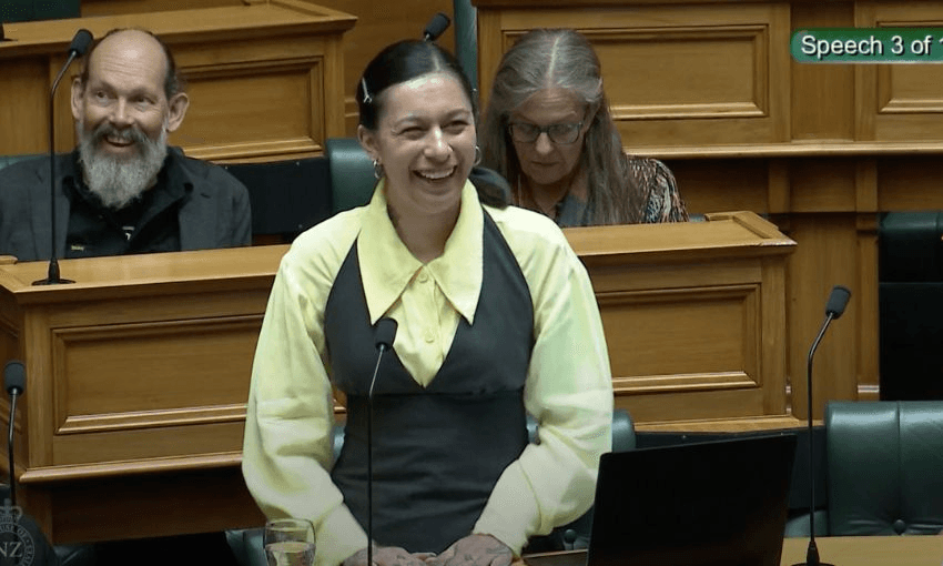 Tamatha Paul standing in the House, laughing and smiling behind a front bench.