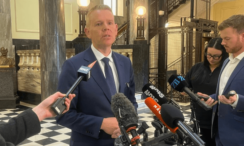 Chris Hipkins stand in front of a row of microphones on parliament's tiles to take questions.