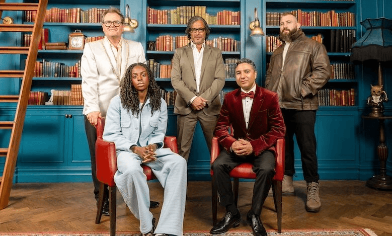 Five celebrities starring in The Celebrity Traitors UK sit and stand in a library