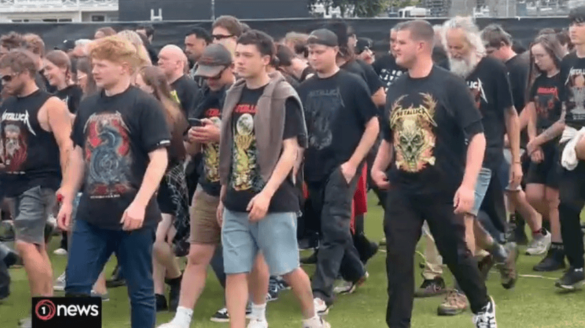 A group of fans wearing Metallica t-shirts walk on some grasss