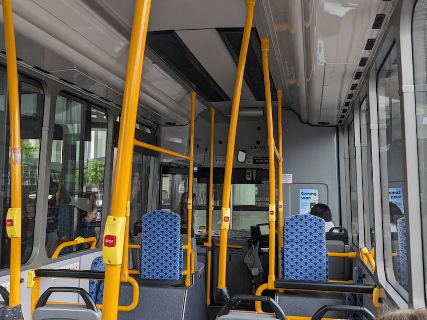 a bus with yellow poles and stop buttons and a small 'coming soon' sign about Motu Move which someone forgot to remove