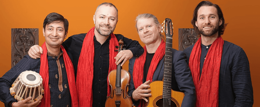 A photo of four men wearing red scarves and holding instruments: they are all smiling.